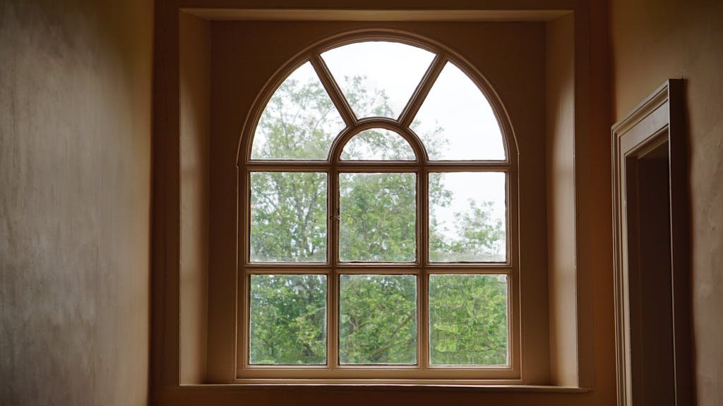 An elegant arched window design framing a lush green view of trees outside. Interior shot.